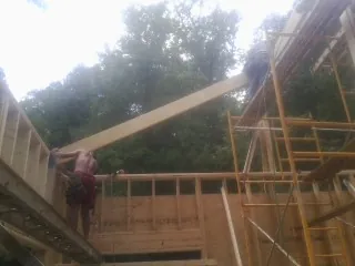 Carpenter raising a rafter beam on a new second story frame in Somerset
